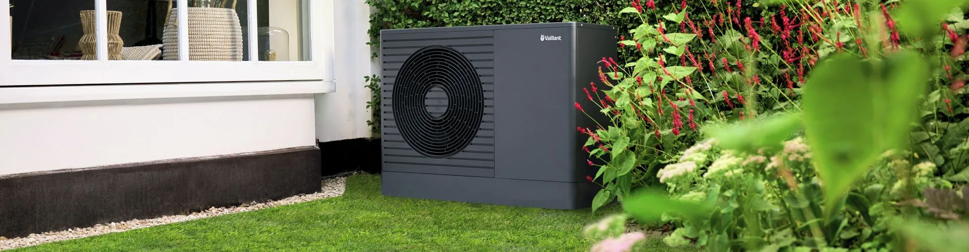 Eine dunkelgraue Wärmepumpe von Vaillant steht im Garten vor einem modernen Einfamilienhaus.