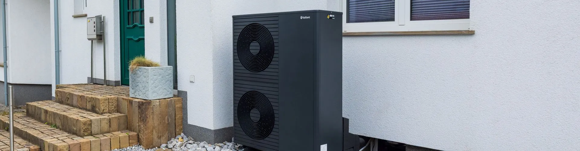 Eine Wärmepumpe des Modells arothermplus von Vaillant steht vor einem Altbau auf dem Kiesbett.