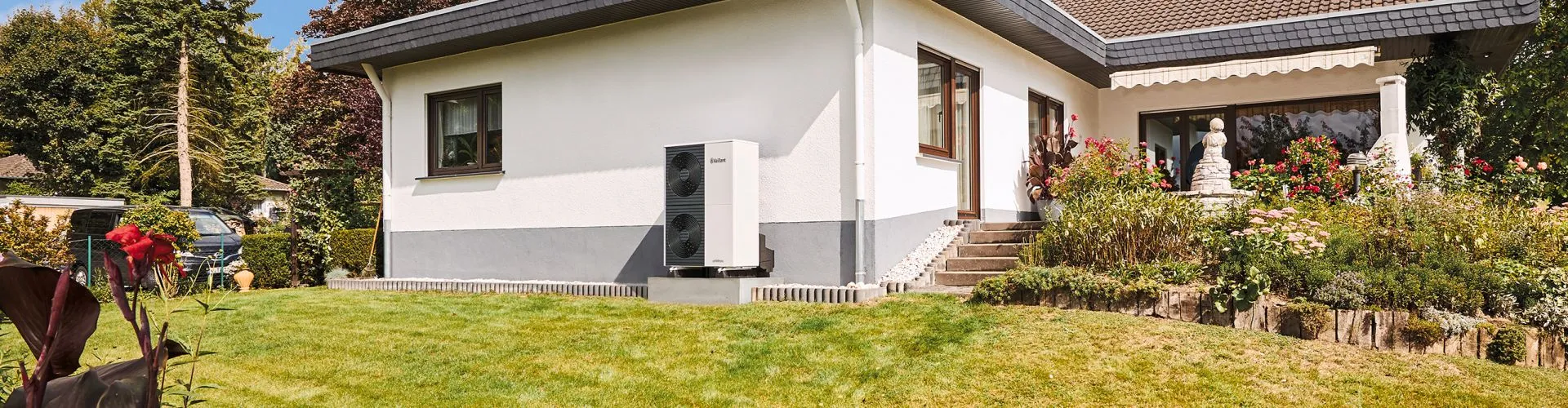 Eine Wärmepumpe des Modells arothermplus von Vaillant steht vor einem Altbau auf dem Kiesbett.