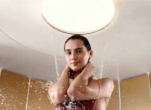 Eine Frau steht unter einer luxuriösen runden Duschbrause, während das Wasser sanft auf sie herabregnet.