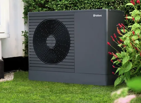 Eine dunkelgraue Wärmepumpe von Vaillant steht im Garten vor einem modernen Einfamilienhaus.