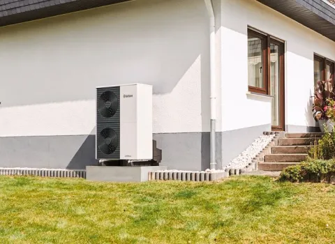 Eine Wärmepumpe von Vaillant steht vor einem Einfamilienhaus im Garten.