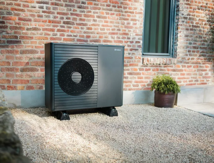 Eine moderne Vaillant-Wärmepumpe steht vor einem Backstein-Altbau.