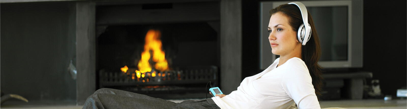 Frau_Wohnzimmer_Kamin_Kopfhörer_Header_2024_1600x430px